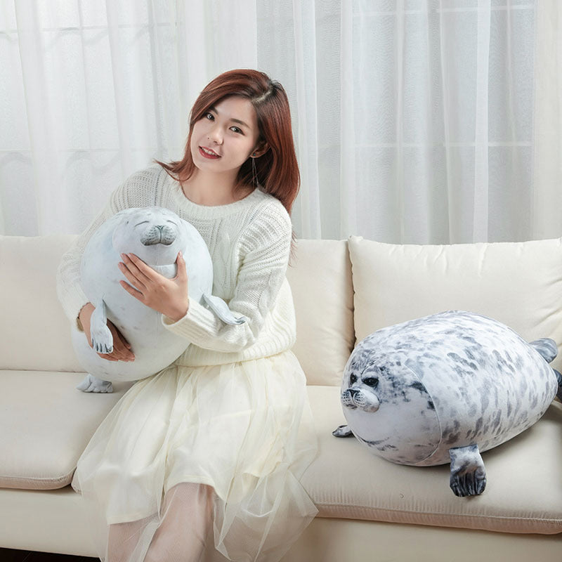 A woman is sitting on a sofa holding a white plush stuffed toy shaped like a seal.