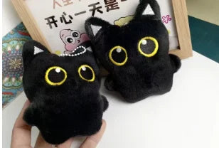 A pair of black cat plush toys with yellow eyes displayed next to a wooden frame.