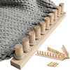 A wooden knitting loom with cylindrical wooden pegs and a knitted gray blanket shown in a diagonal view.