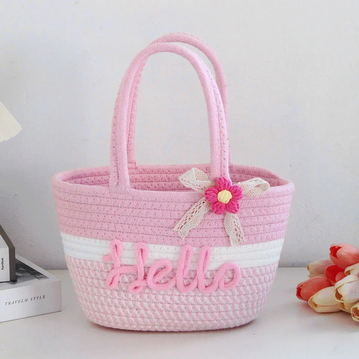 A pink braided cotton tote bag with a floral embellishment and white stripes.
