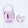 A pink personalized baby pacifier with a crown design and storage case.