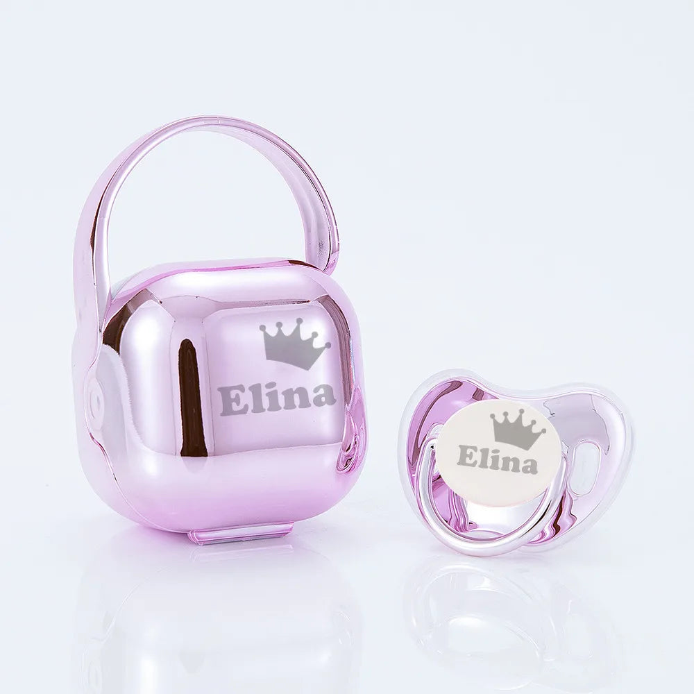 A pink personalized baby pacifier with a crown design and storage case.