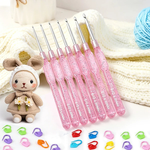 A set of seven pink crochet hooks with counting clips displayed on a white background next to a knitted blanket and a small s