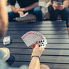 Une main tient un jeu de cartes rouge et blanc sur une table en bois sombre.