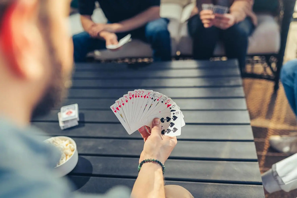 Une main tient un jeu de cartes rouge et blanc sur une table en bois sombre.