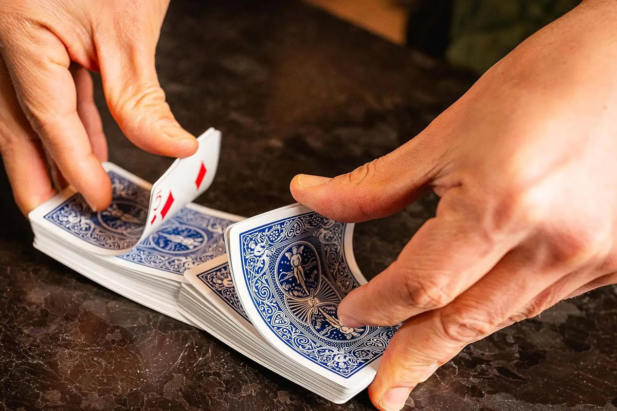 Une main tient une pile de cartes bleues, dont une montre l'As de pique.