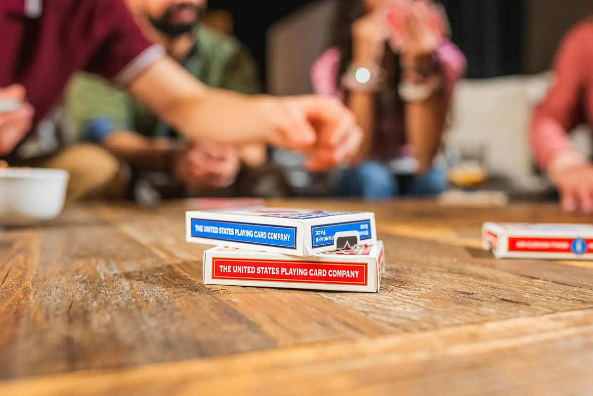Une table en bois présentant plusieurs boîtes de cartes à jouer de la société United States Playing Card Company et des perso