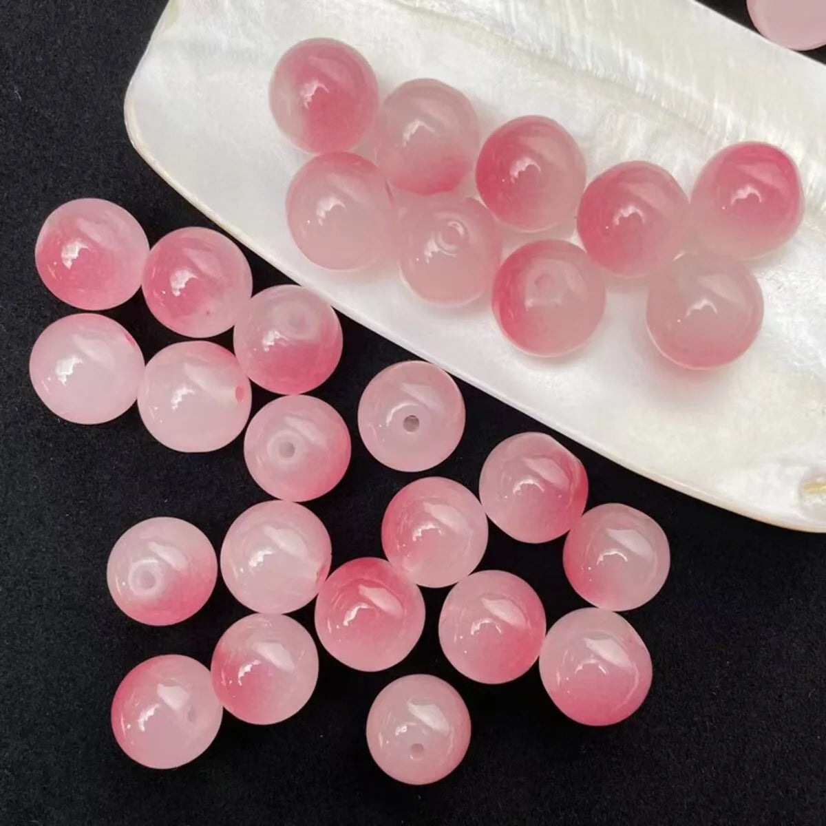 A collection of pink and rosy glass round beads are displayed on a white oval tray.