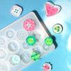 A silicone button resin casting mold with various pink, green, and white colored buttons and components arranged on a light b