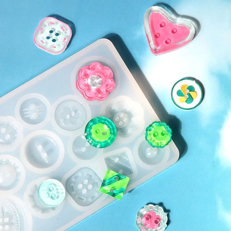 A silicone button resin casting mold with various pink, green, and white colored buttons and components arranged on a light b