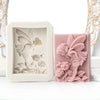 A pink silicone soap mold featuring a 3D design of a flower, rose, and butterfly.