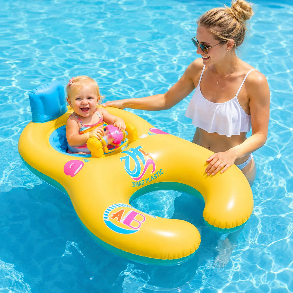 A woman is floating a baby in a yellow inflatable pool lounger with a sun canopy in blue water.
