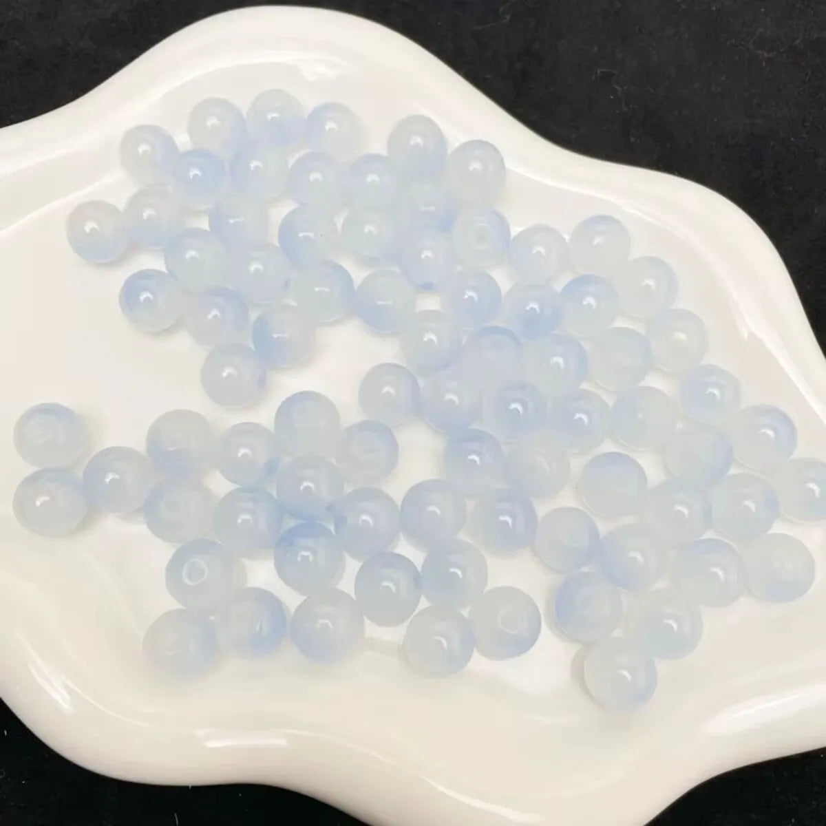 A pile of light blue and clear glass round beads for jewelry making on a white surface.