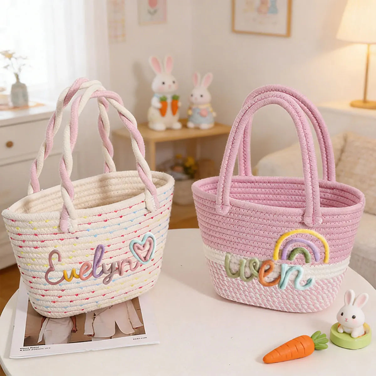 A pink braided cotton tote bag with a rainbow design sits next to a white one, with an carrot decoration.