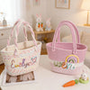 A pink braided cotton tote bag with a rainbow design sits next to a white one, with an orange carrot nearby.