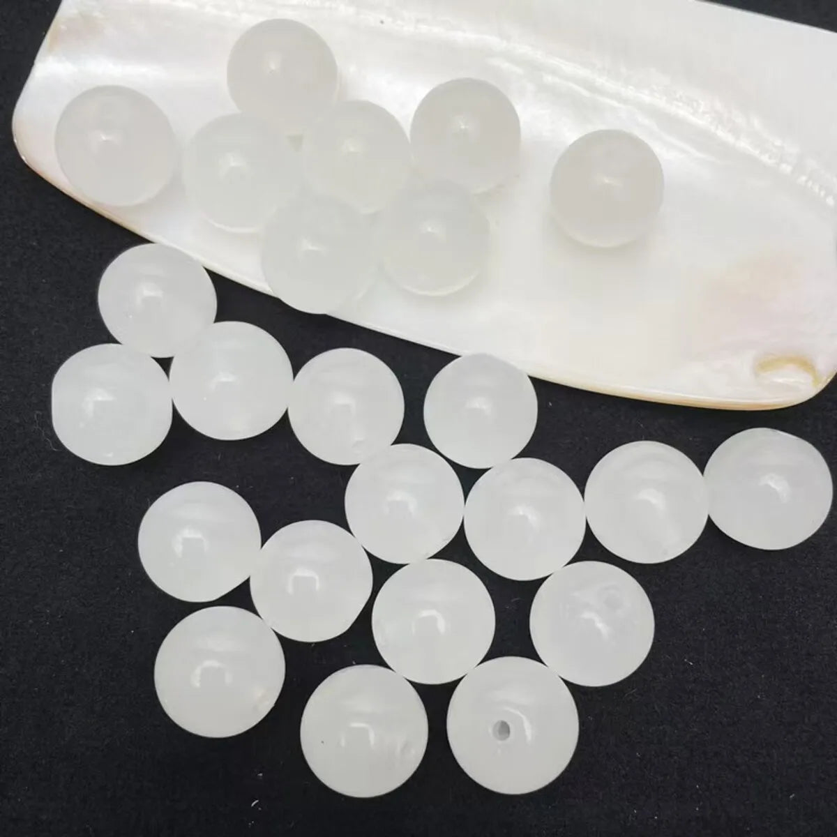 A translucent white plastic tray holds a pack of round, clear glass beads for jewelry making.
