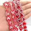 A hand holds a string of red and pink heart-shaped lampwork glass beads for jewelry making.