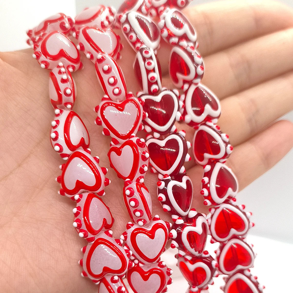 A hand holds a string of red and pink heart-shaped lampwork glass beads for jewelry making.