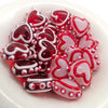 A pile of red and pink heart-shaped lampwork glass beads for jewelry making arranged in a white bowl.