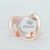 A personalized baby pacifier with a crown design and storage case in rose gold metal.
