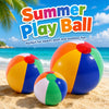 A colorful rainbow inflatable beach ball resting on the sand with a blue ocean and sky in the background.