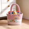 A pink braided cotton tote bag decorated with a rainbow design and featuring a yellow stuffed animal.