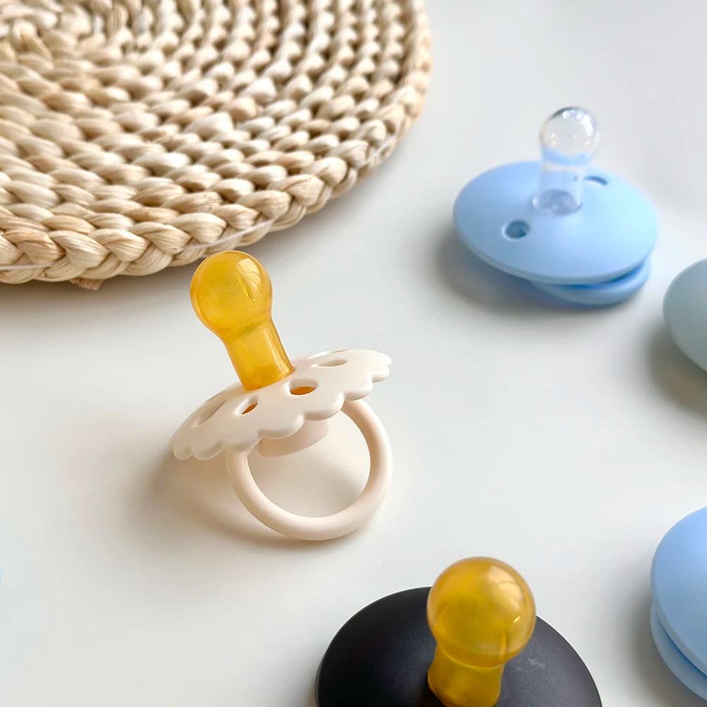 A natural latex baby pacifier in yellow and white is shown next to a woven mat and blue silicone components.