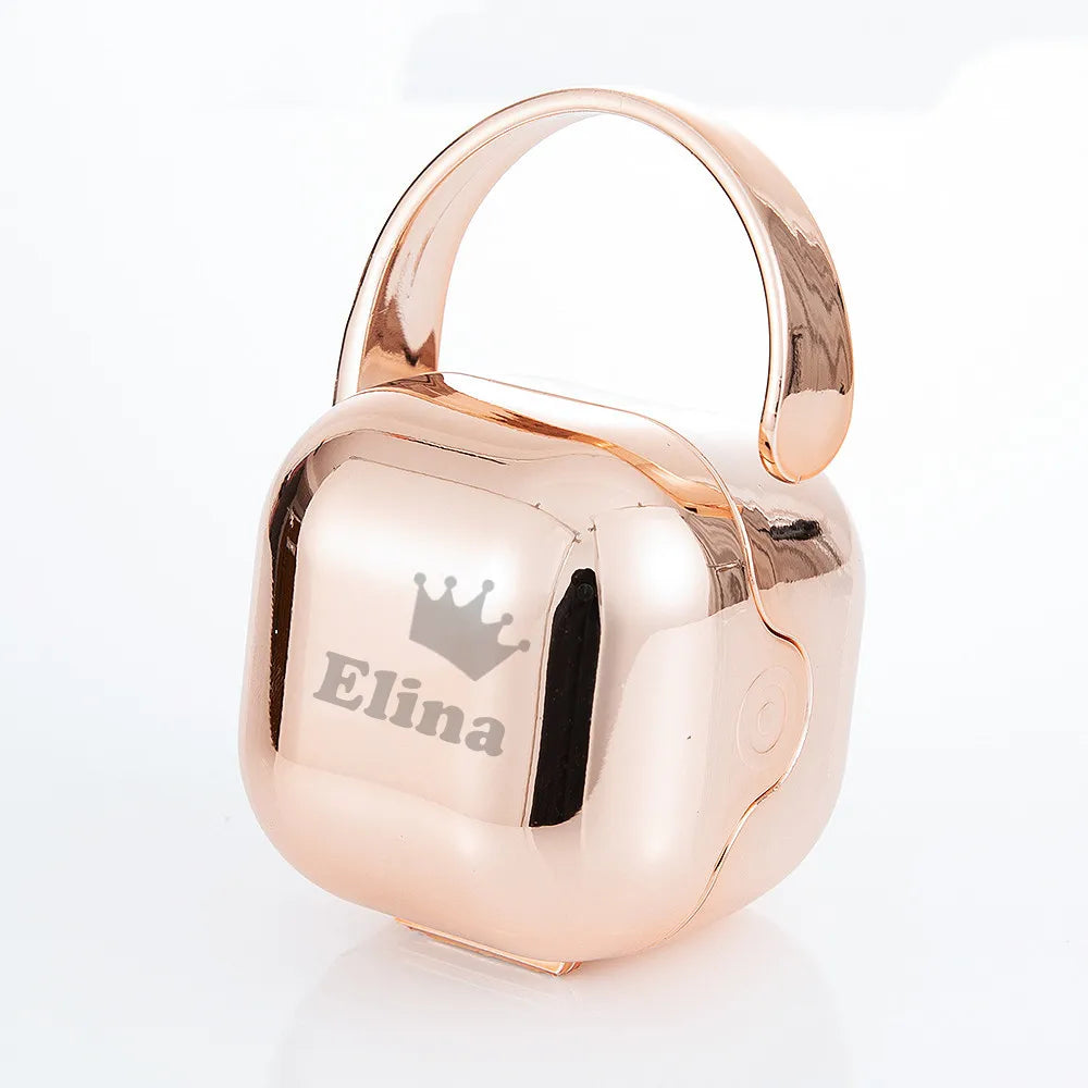 A rose gold baby pacifier with a crown design is shown in its storage case.