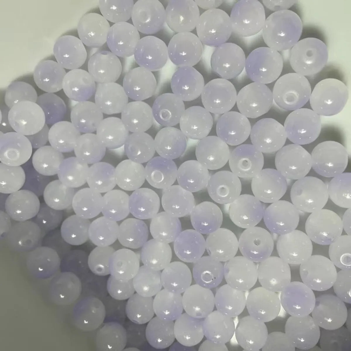 A close-up view of a 50-pack of dual-color glass round beads for jewelry making, featuring light purple and clear beads.