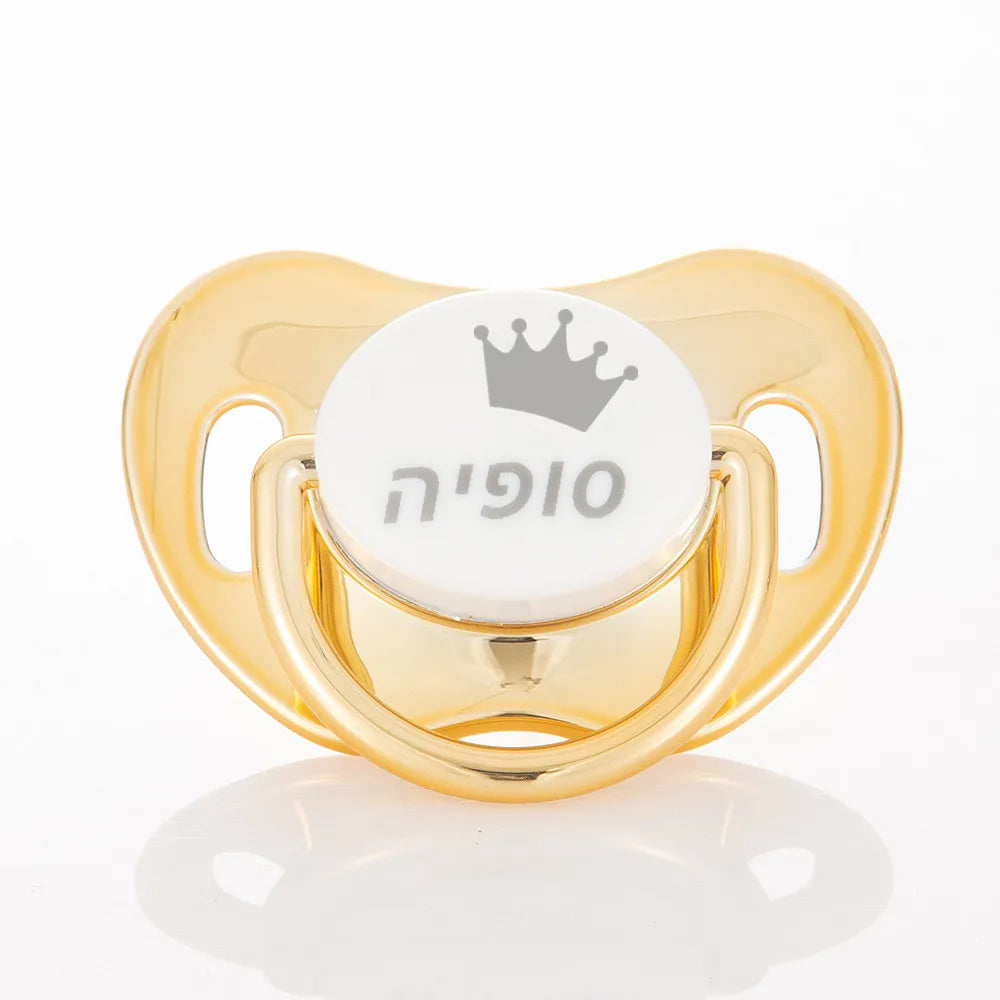 Gold-colored pacifier storage case with a white pacifier featuring a silver crown design