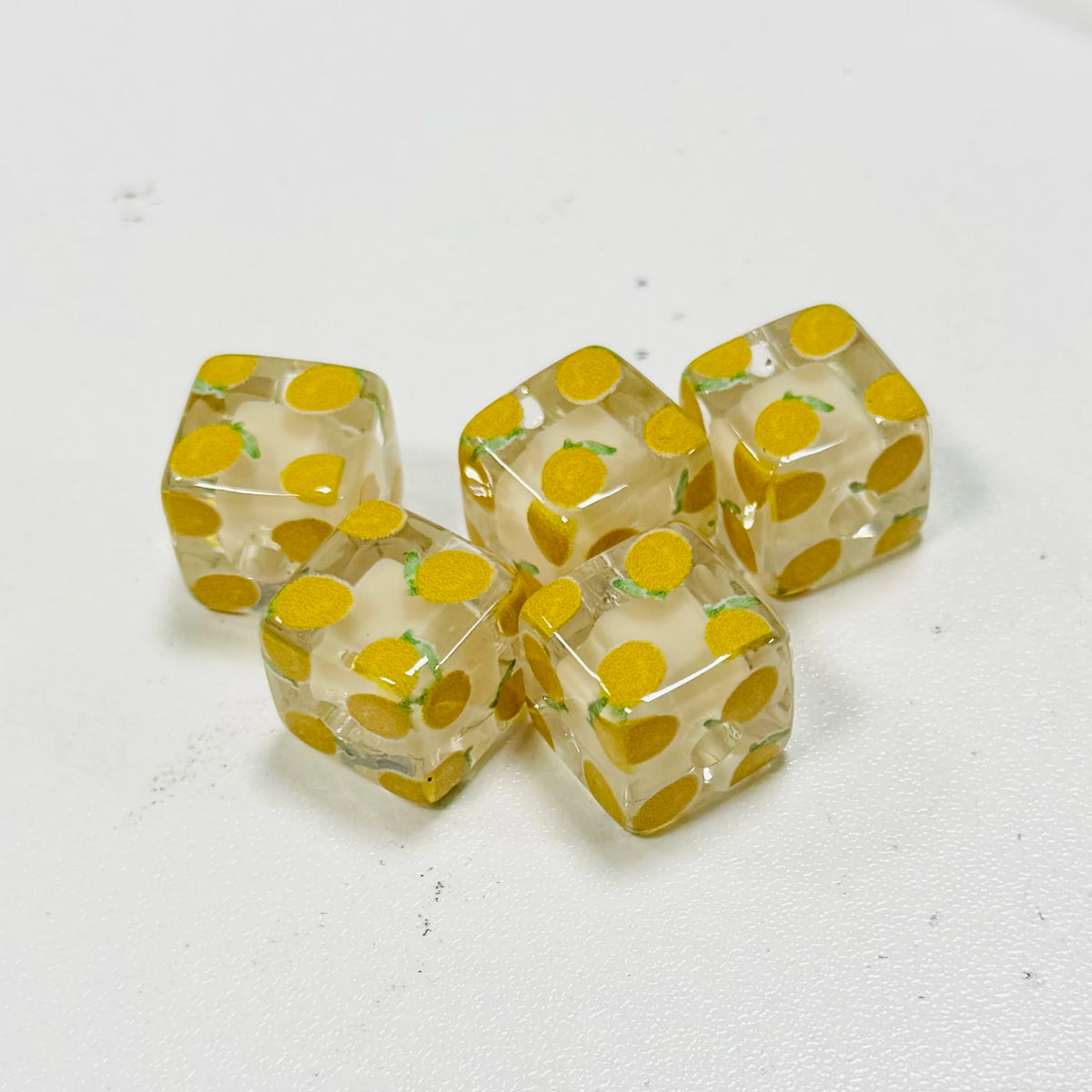 A collection of small, square resin beads with a floral pattern in yellow and green tones.