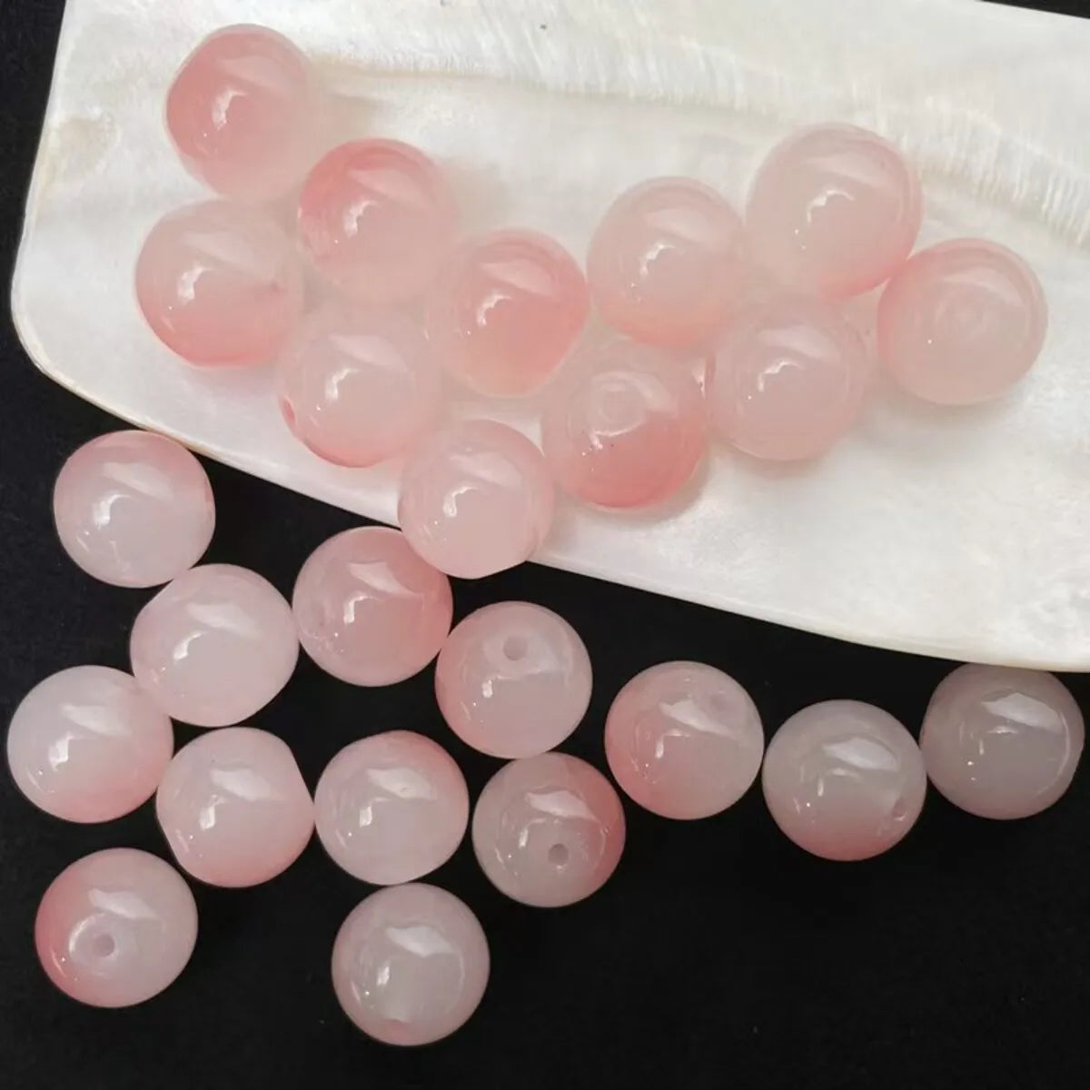 A collection of pink and clear glass round beads arranged on a white oval tray.