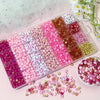 A variety of pink, red, and white acrylic beads with gold accents are displayed in a clear plastic box.