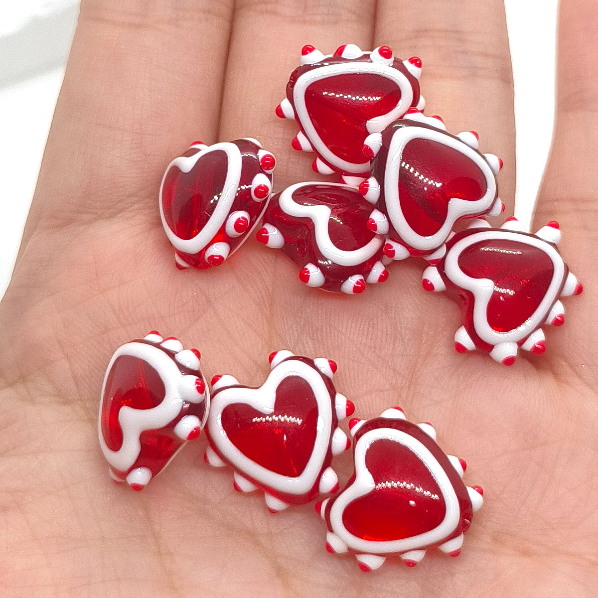 A collection of red heart-shaped lampwork glass beads for jewelry making displayed on a hand.
