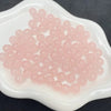 A pile of pink glass round beads for jewelry making is displayed on a white dish.