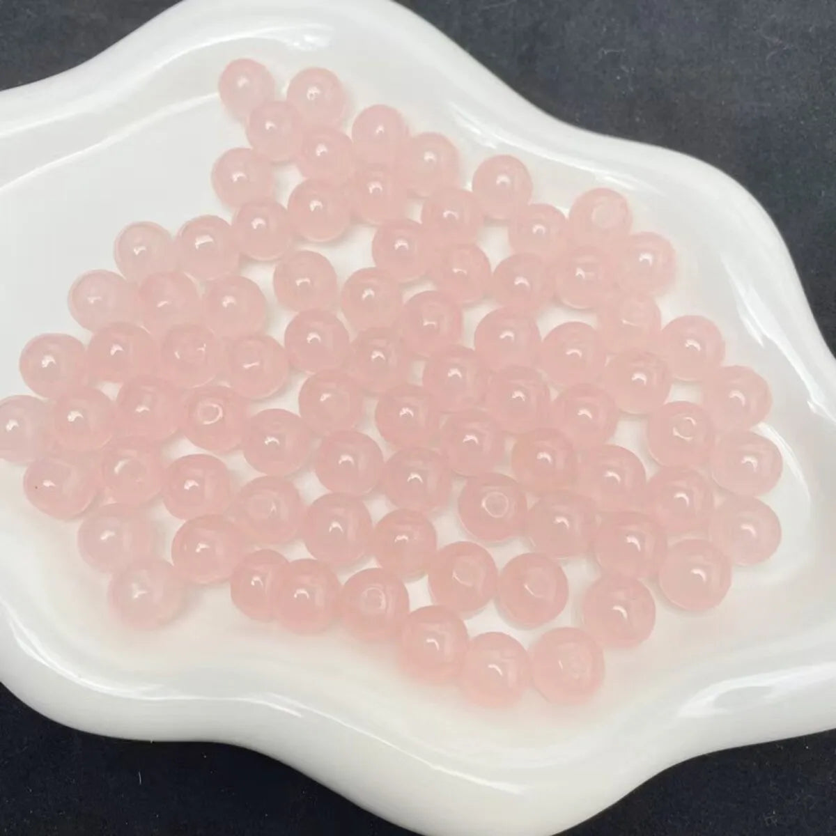 A pile of pink glass round beads for jewelry making is displayed on a white dish.