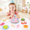 A wooden pretend play birthday cake set with various food shapes and a small cake on a white plate.