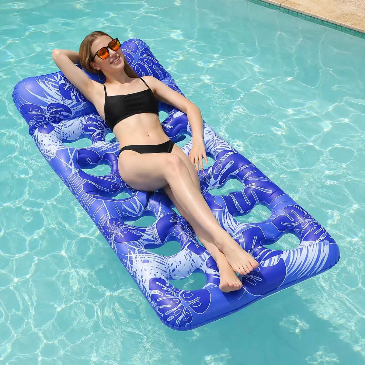 A woman relaxing on a blue inflatable pool float with a headrest in clear water.