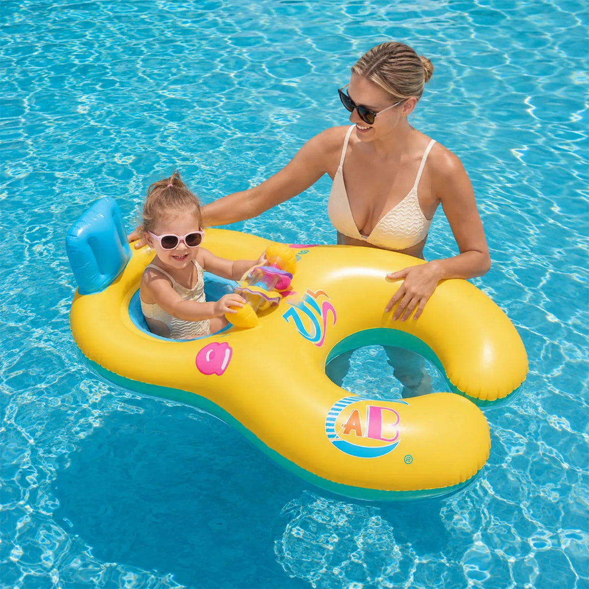 A woman is lying on a yellow inflatable pool lounger with a child in a bright blue swimming pool.