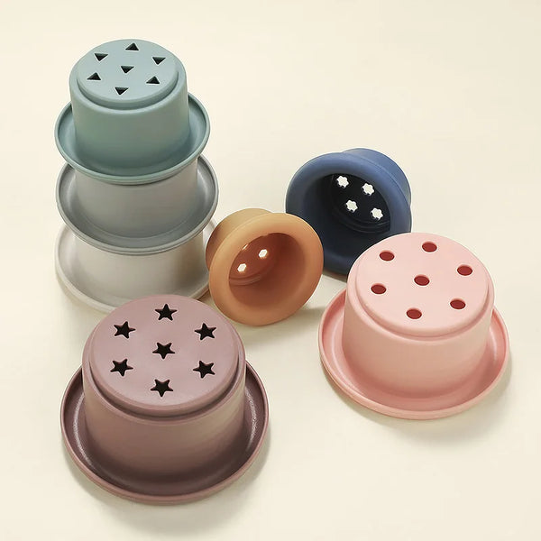 A collection of silicone stacking cups in various muted pastel colors, including blue-green, gray, and pink.