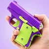 A hand holds a purple and lime green fidget pistol toy with burst slide action.