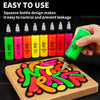 A hand squeezes a neon green bottle of acrylic paint onto a wooden board with colorful paint designs.
