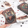 A hand holds a vintage cat illustration playing card deck with a dark, ornate design on a white background.