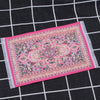 A pink and purple handwoven Turkish style miniature carpet mat displayed on a black checkered surface.