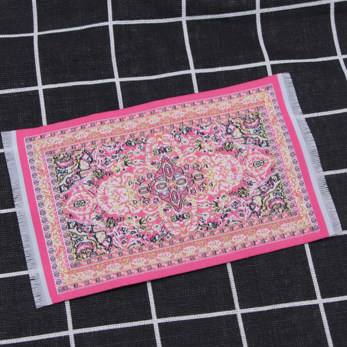 A pink and purple handwoven Turkish style miniature carpet mat displayed on a black checkered surface.