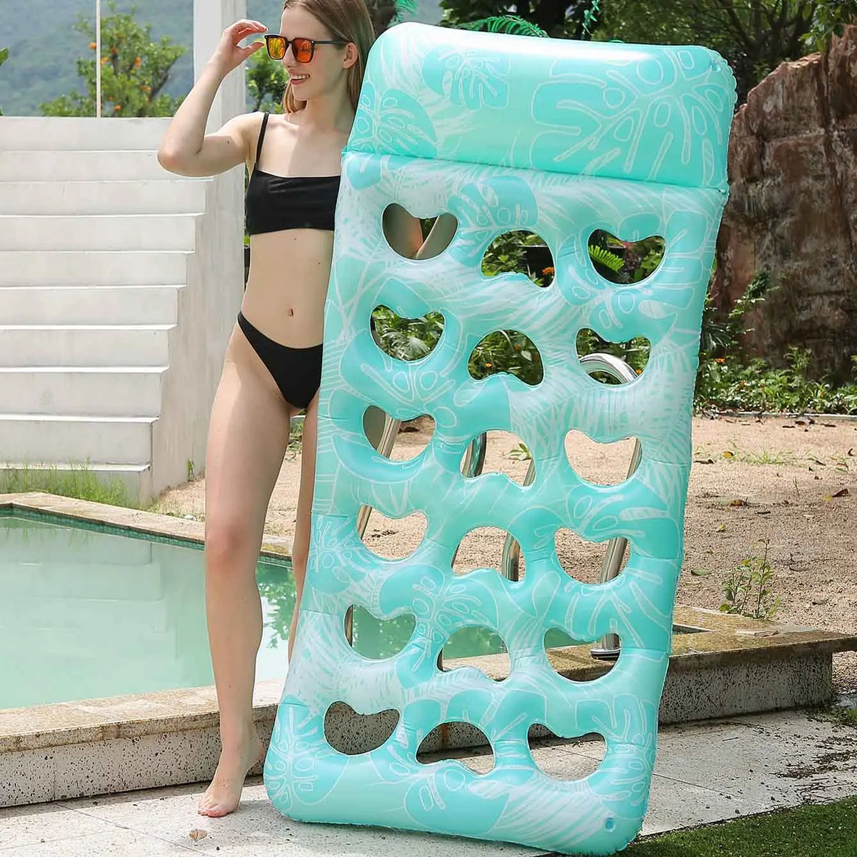 A woman is standing next to a light blue inflatable pool float with a headrest in an outdoor setting.