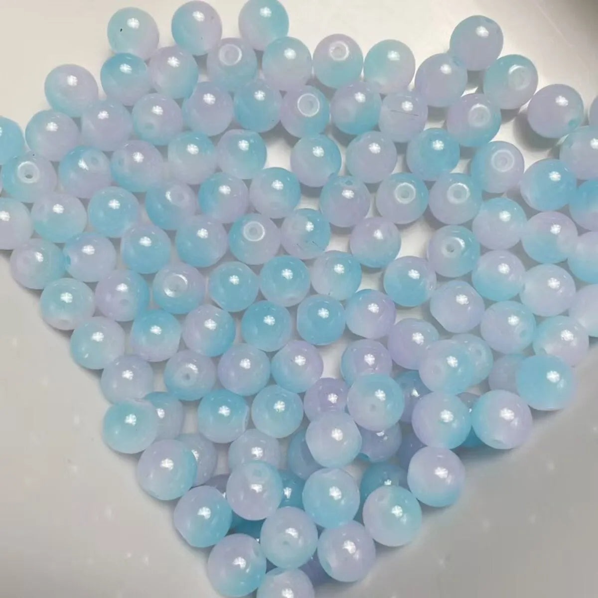 A pile of dual-color glass round beads in light blue and lavender shades.