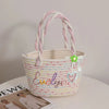 A white braided cotton tote bag with pink yarn handles and a heart charm