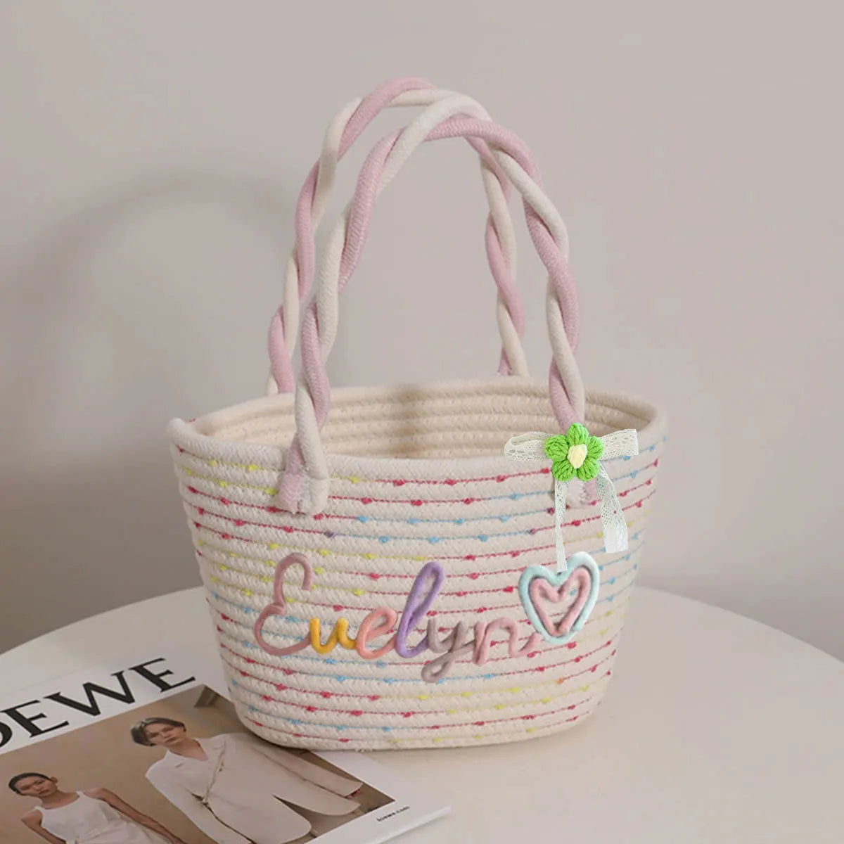 A white braided cotton tote bag with pink yarn handles and a heart charm