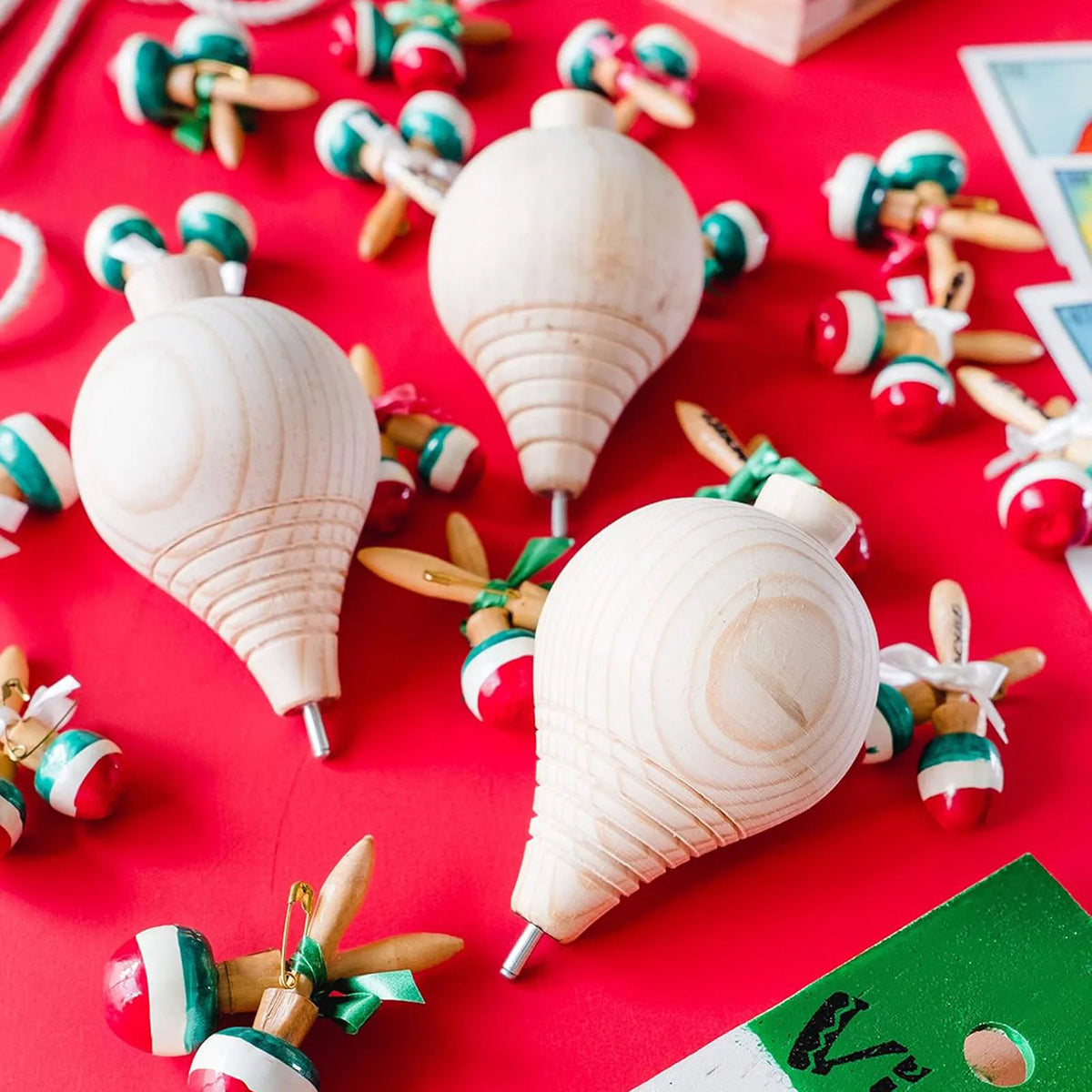 Three unfinished wooden spinning tops with steel points are displayed on a red surface for a paint your own craft toy project